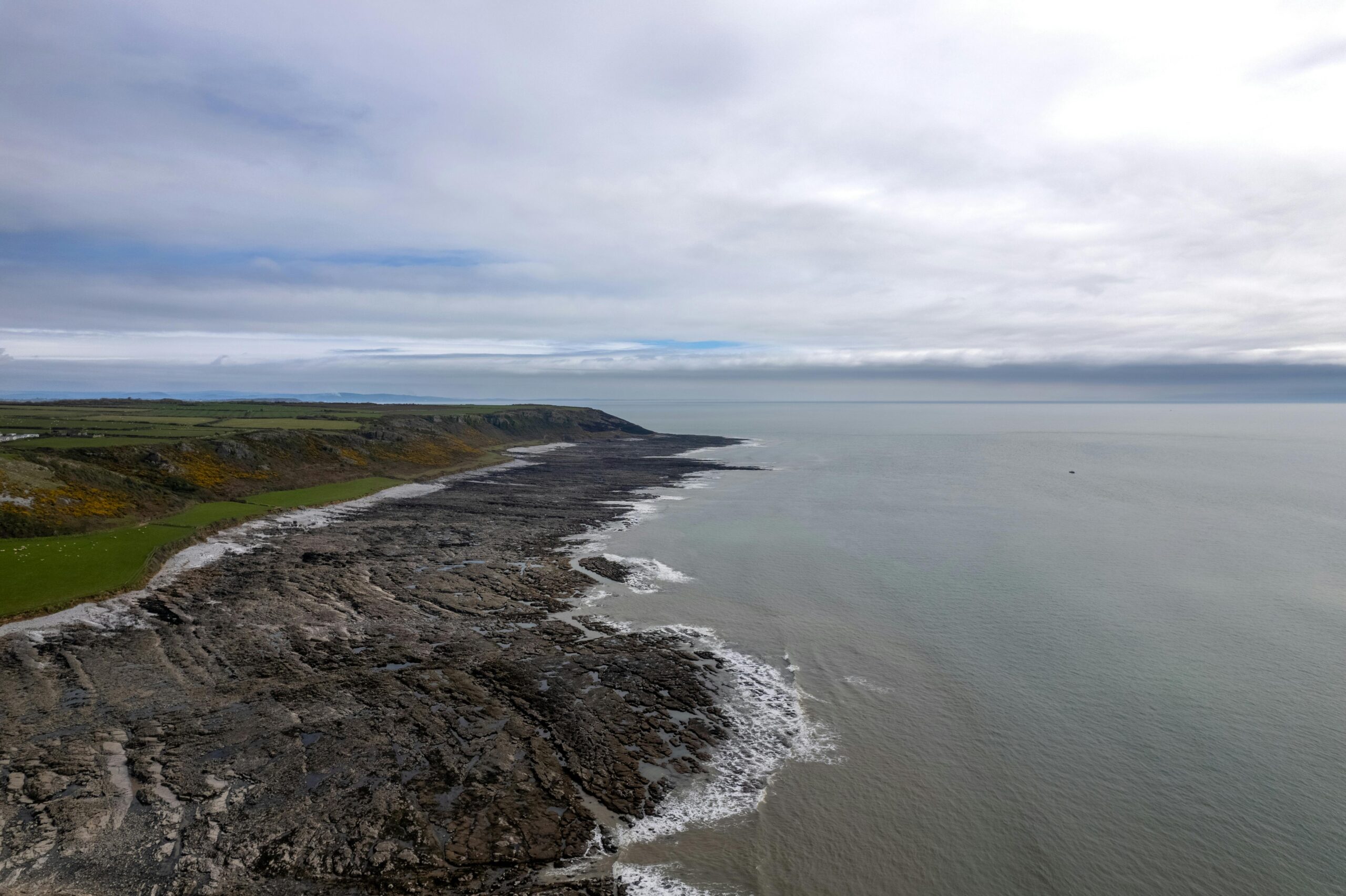 Drone shot capturing the rugged coastline of Slade, Wales, under a cloudy sky, perfect for landscape enthusiasts.